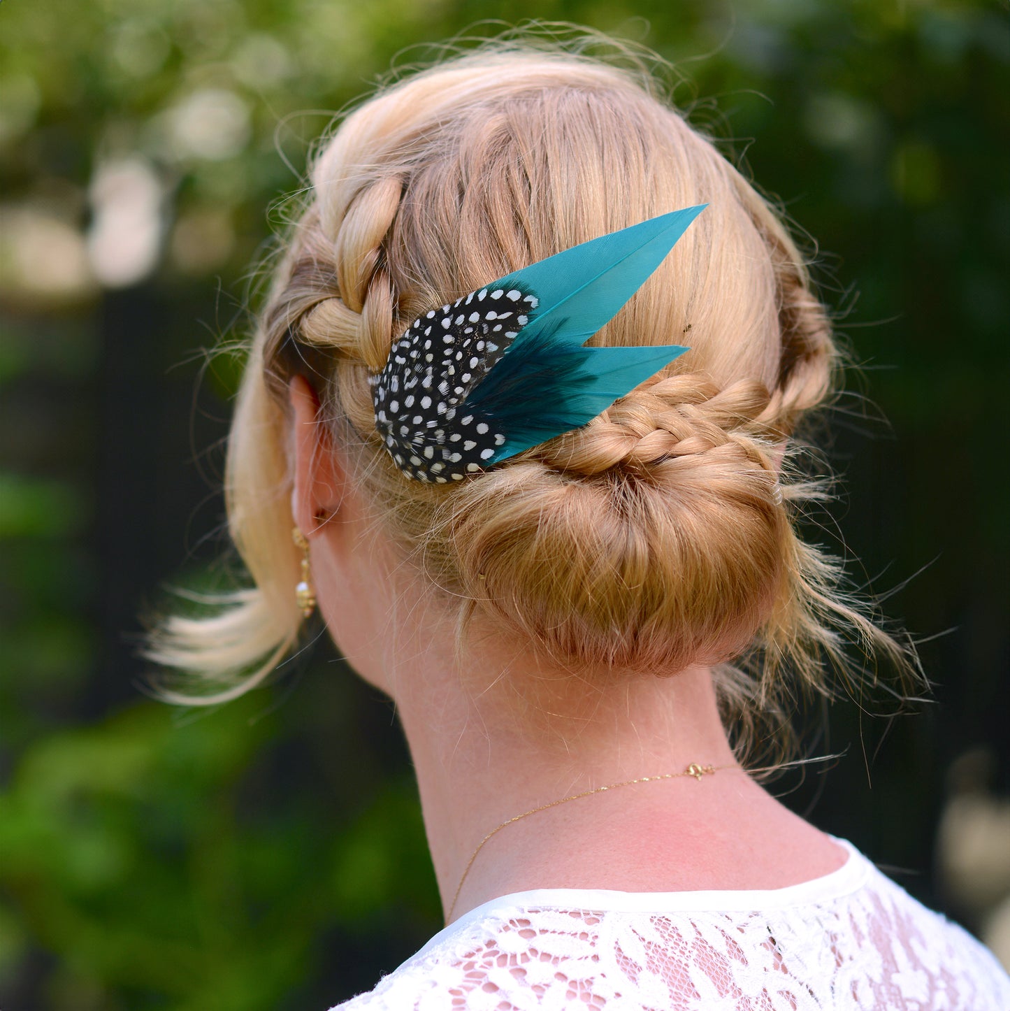 Person with braided hair and turquoise blue decorative feather hair clip against a blurred green background
