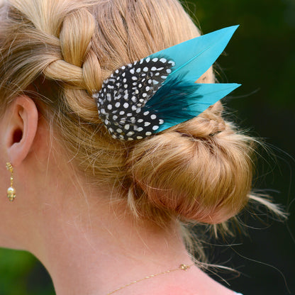 Person with braided hair wearing a decorative hair clip with teal and polka dot feathers.