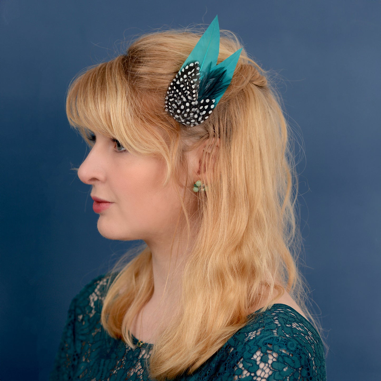 Woman with a teal and polka dot feathered hair accessory against a blue background