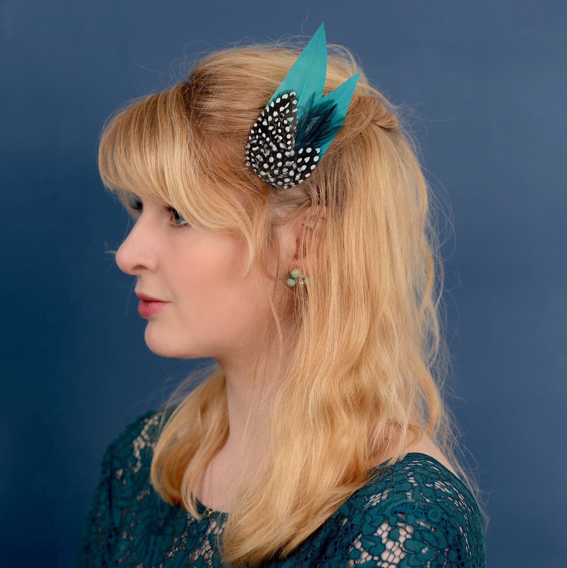 Woman with a teal and polka dot feathered hair accessory against a blue background